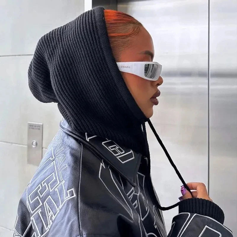 Person in black knit balaclava, hooded jacket, and futuristic sunglasses with orange hair