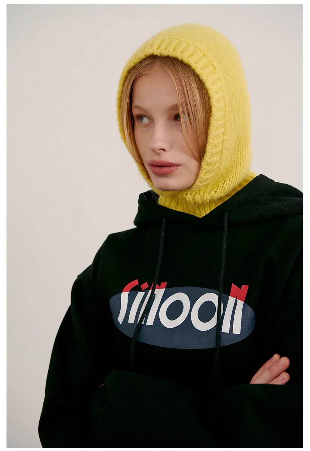 Person wearing a black knitted balaclava hood with Moon text and bright yellow hood