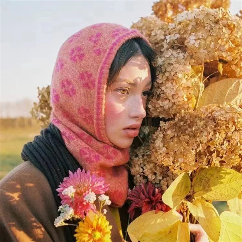 Woman with a pink floral headscarf holding flowers, showcasing a pink knitted balaclava